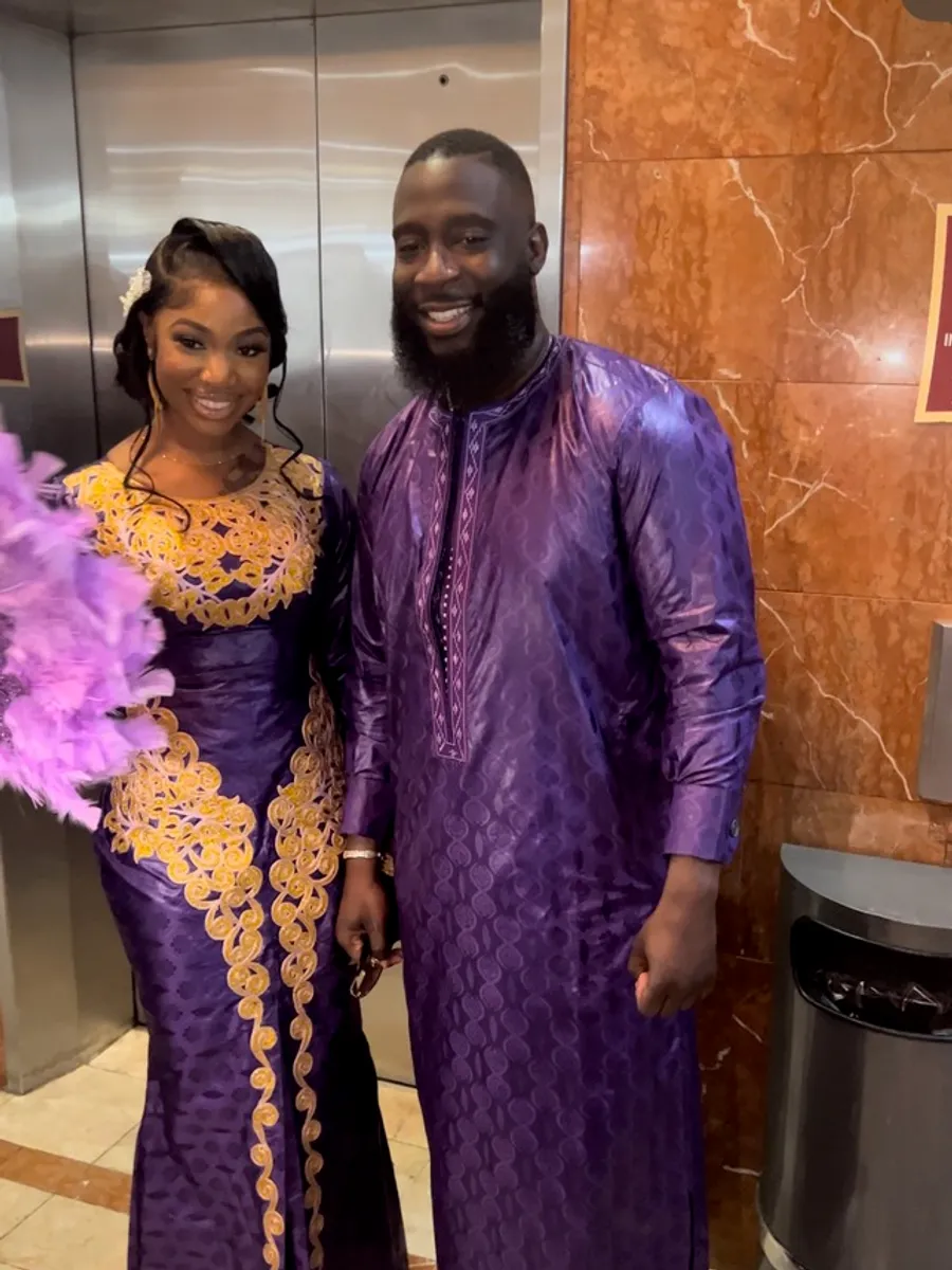 A couple dressed for a celebration in coordinated purple: his kaftan in a tone-on-tone weave, her gown embroidered in gold.