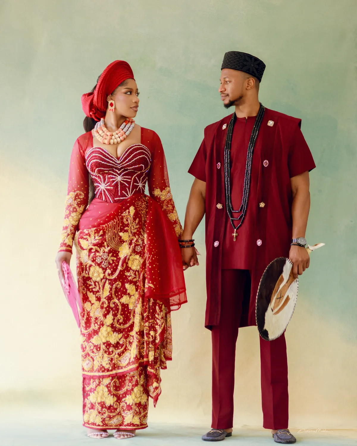 A pre-wedding studio portrait: the couple hand in hand in coordinated red and gold traditional attire.