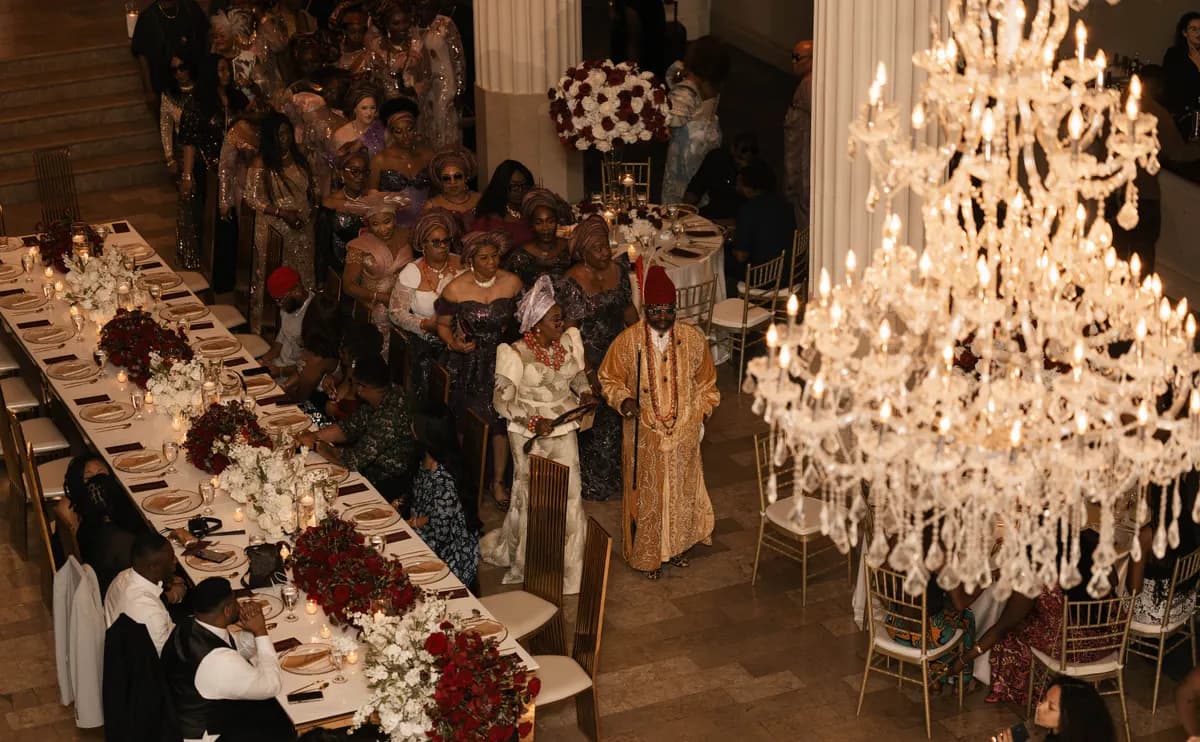 A reception in full swing: long tables of red roses beneath crystal chandeliers, with the guests seated.