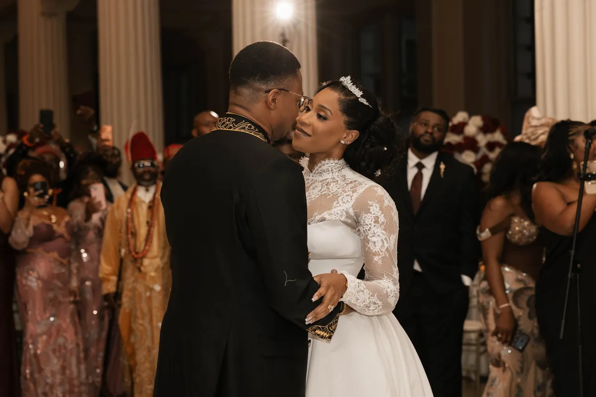 The first dance at a reception, guests looking on: the groom in the black and gold suit, the bride in lace.